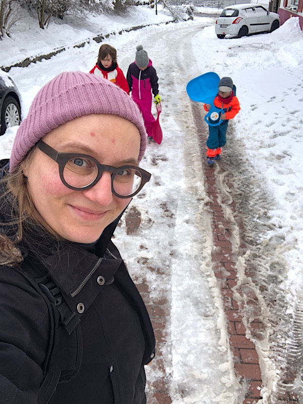 Frau im Vordergrund mit 3 Kindern, die im Schnee spielen