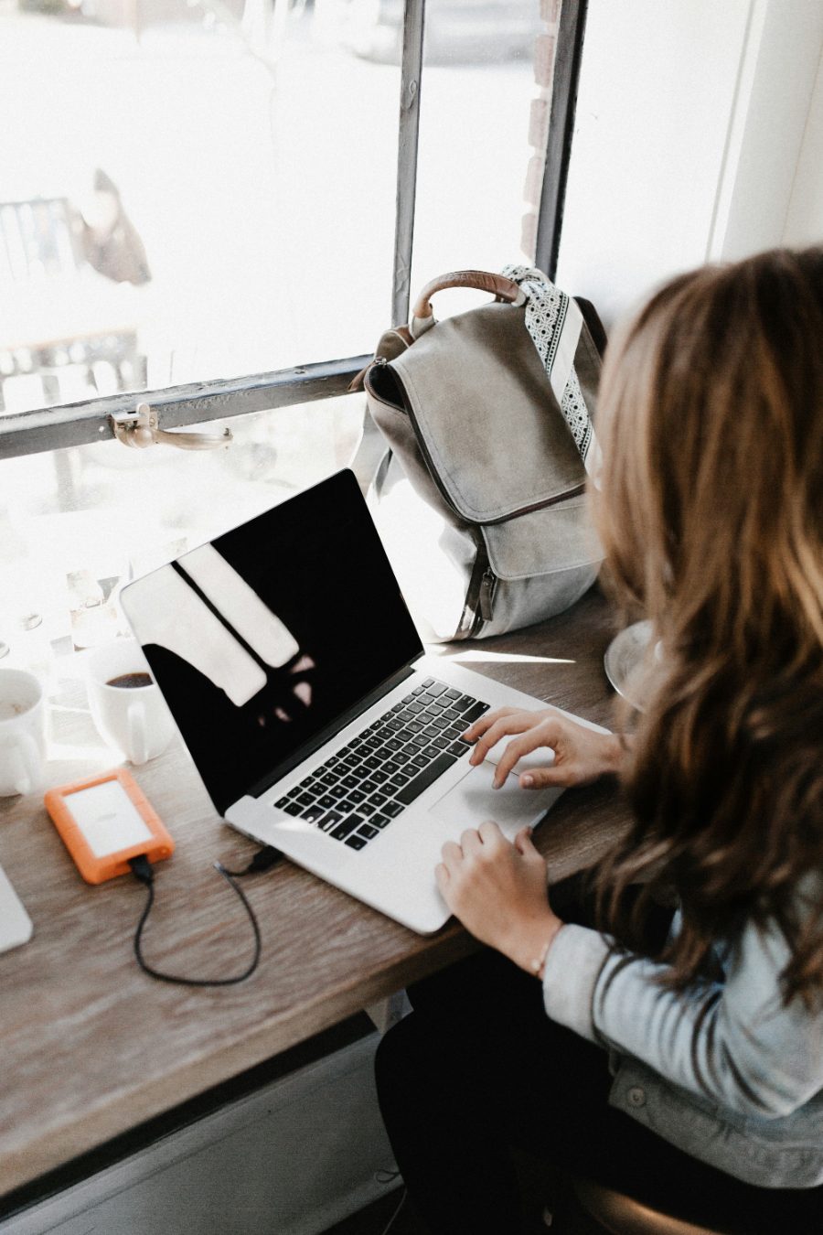 Bloggerin arbeitet mit Laptop am Fenster eines Cafés